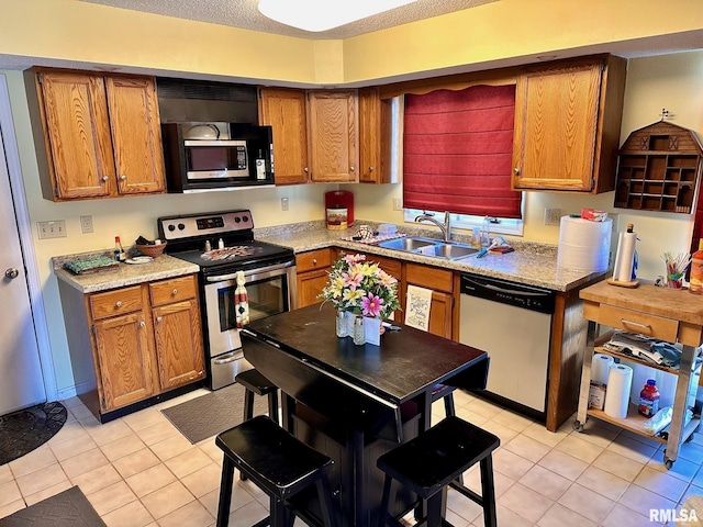 kitchen featuring stainless steel appliances, brown cabinetry, a sink, and light stone countertops