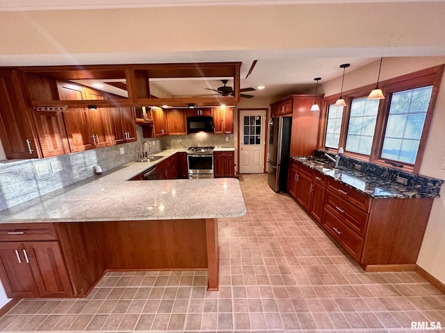 kitchen featuring light stone counters, a peninsula, hanging light fixtures, stainless steel appliances, and a sink