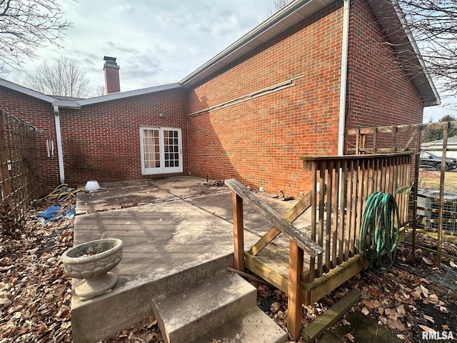 rear view of house with a deck, brick siding, a chimney, and fence