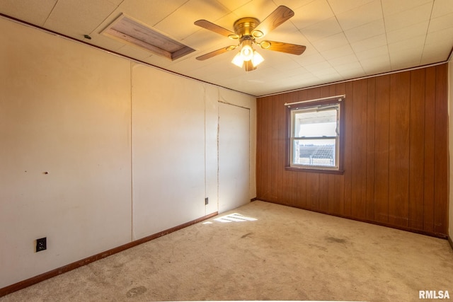 spare room with ceiling fan, wood walls, baseboards, and light colored carpet