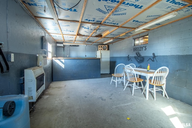 interior space with heating unit, concrete block wall, concrete floors, and freestanding refrigerator