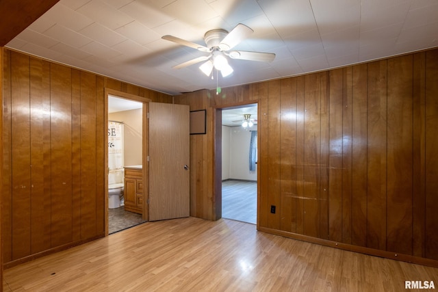 unfurnished bedroom featuring ensuite bathroom, light wood finished floors, and wood walls