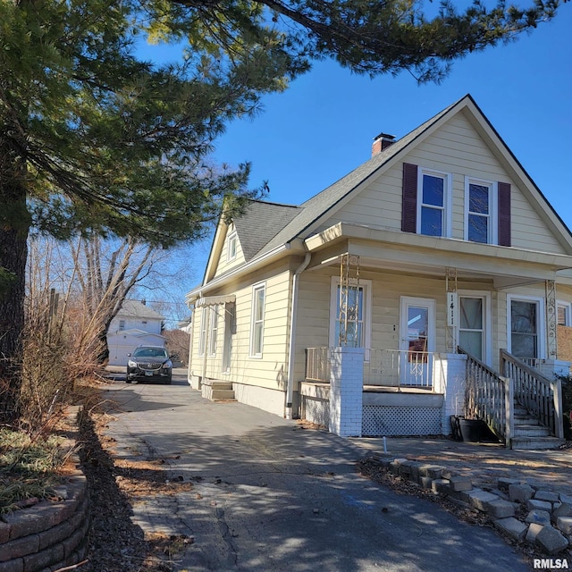 view of front of house with covered porch, driveway, roof with shingles, and a chimney