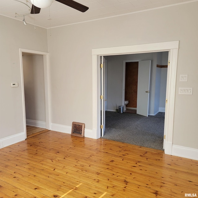 unfurnished room with ceiling fan, wood-type flooring, visible vents, and baseboards