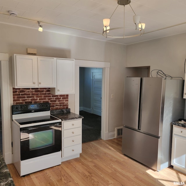 kitchen with light wood finished floors, freestanding refrigerator, white cabinets, dark stone counters, and range with electric cooktop