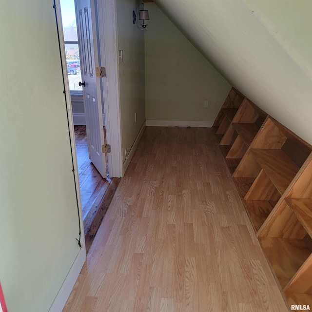 corridor with lofted ceiling, light wood-style flooring, and baseboards