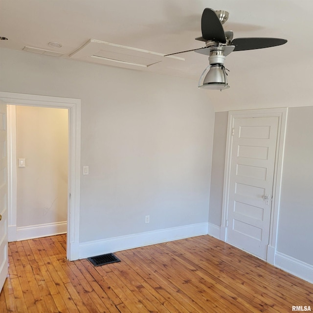 empty room with light wood-style flooring, visible vents, attic access, and baseboards