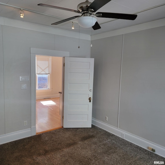 carpeted empty room with rail lighting, ceiling fan, and baseboards