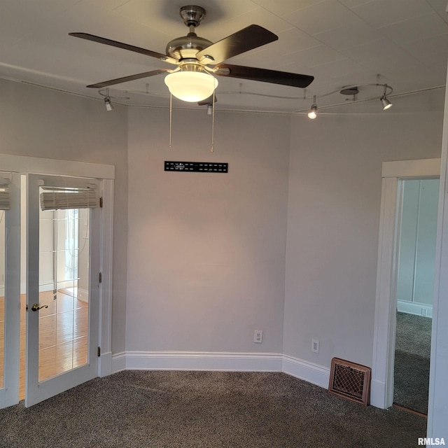 carpeted spare room featuring ceiling fan, track lighting, visible vents, and baseboards