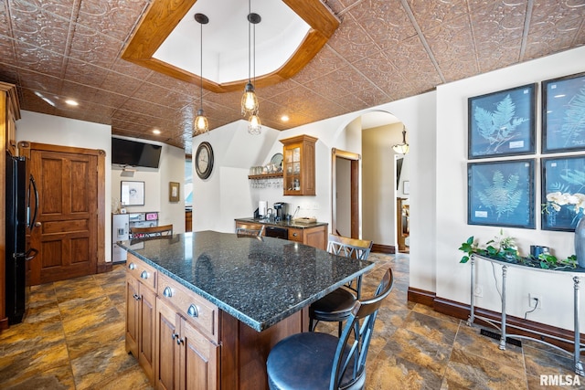 kitchen featuring arched walkways, a breakfast bar, baseboards, freestanding refrigerator, and an ornate ceiling