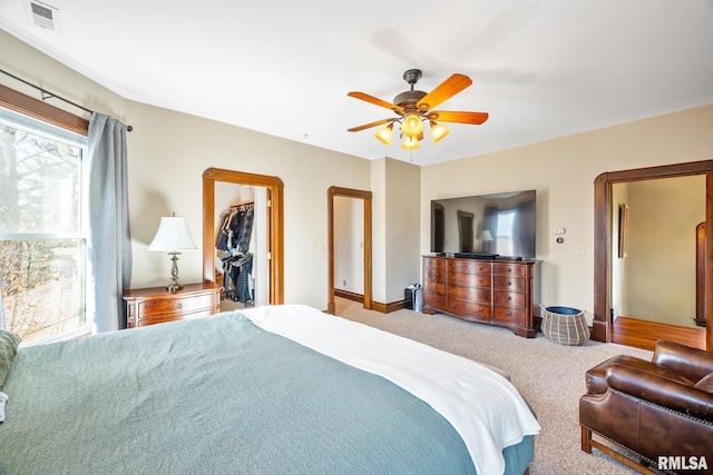 carpeted bedroom featuring visible vents, baseboards, a ceiling fan, a closet, and a walk in closet