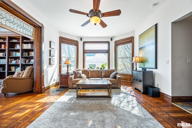 living room with a ceiling fan, baseboards, and wood finished floors