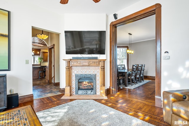 living room featuring crown molding, a fireplace, a ceiling fan, wood finished floors, and baseboards