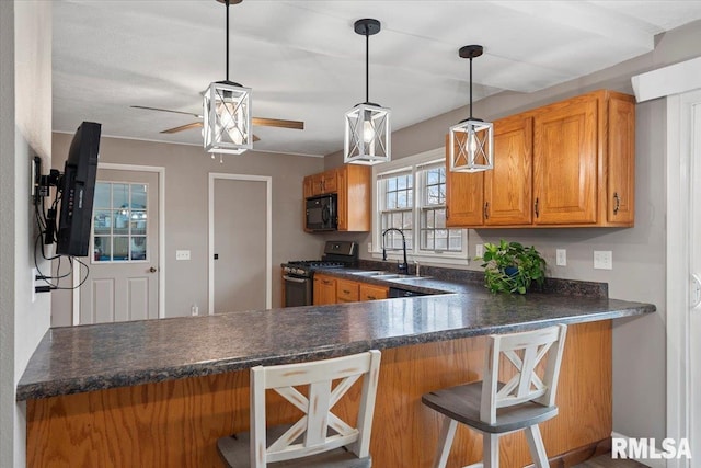 kitchen featuring a sink, dark countertops, brown cabinetry, black microwave, and stainless steel range with gas stovetop