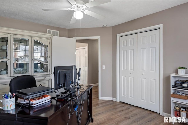 home office featuring visible vents, baseboards, wood finished floors, a textured ceiling, and a ceiling fan