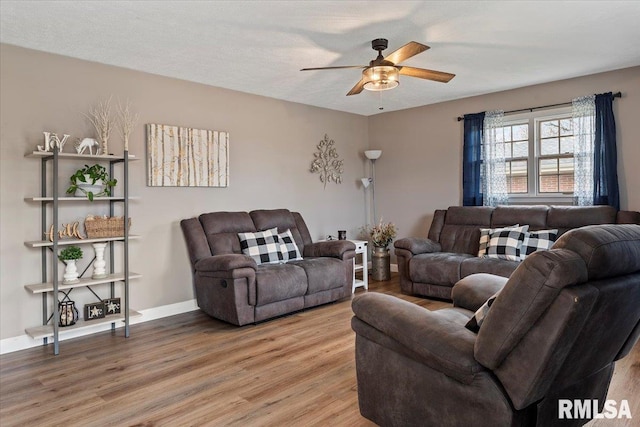 living area with baseboards, light wood-style flooring, and a ceiling fan