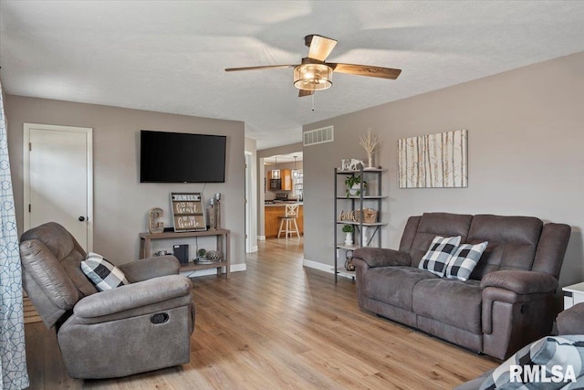 living room with a ceiling fan, baseboards, visible vents, a textured ceiling, and light wood-type flooring