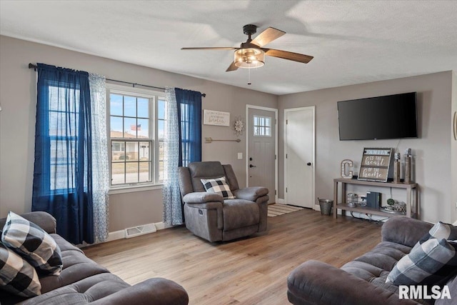 living room featuring visible vents, a textured ceiling, light wood-type flooring, and a ceiling fan