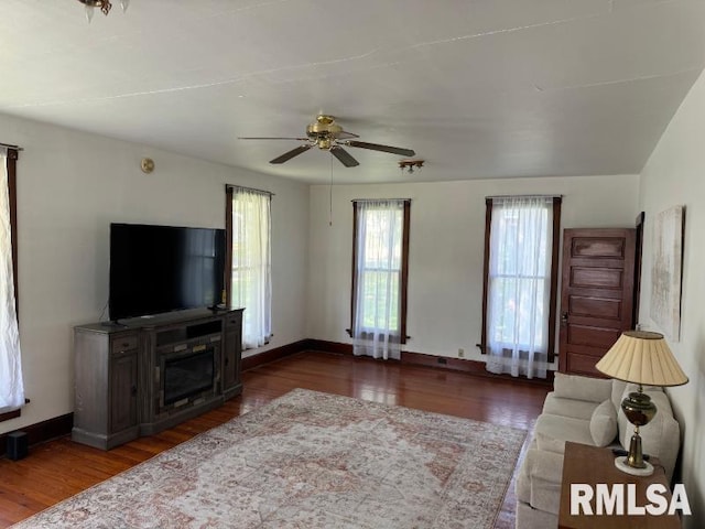 living room with a ceiling fan, baseboards, and wood finished floors