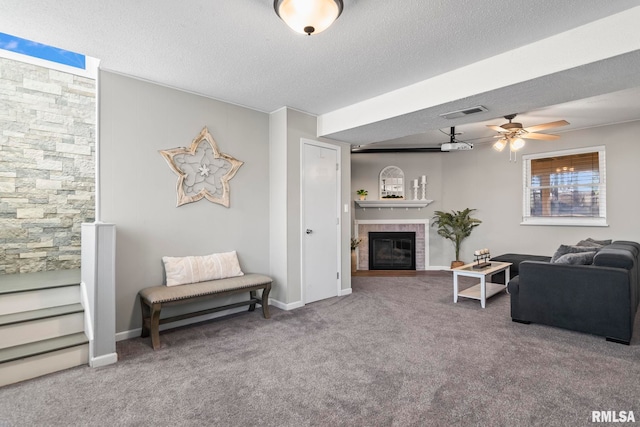 carpeted living room featuring visible vents, baseboards, a textured ceiling, and a glass covered fireplace