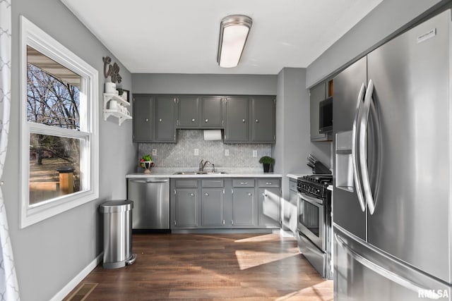 kitchen featuring a sink, decorative backsplash, gray cabinetry, light countertops, and stainless steel appliances