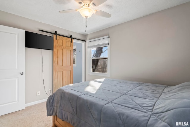 bedroom with baseboards, ceiling fan, light colored carpet, a barn door, and a textured ceiling