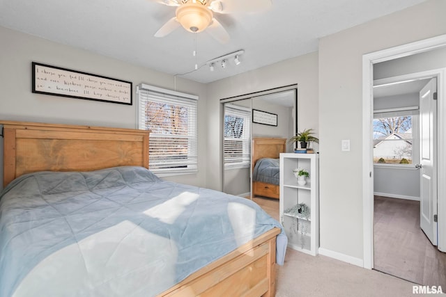 carpeted bedroom featuring track lighting, ceiling fan, and baseboards