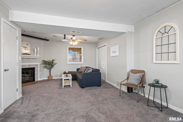 living area featuring visible vents, a textured ceiling, carpet flooring, ceiling fan, and a tile fireplace