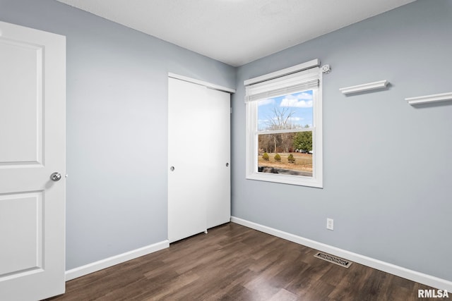 unfurnished bedroom featuring visible vents, baseboards, a closet, and dark wood-style floors