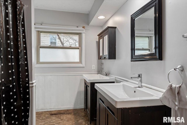 bathroom featuring a wainscoted wall, visible vents, two vanities, and a sink