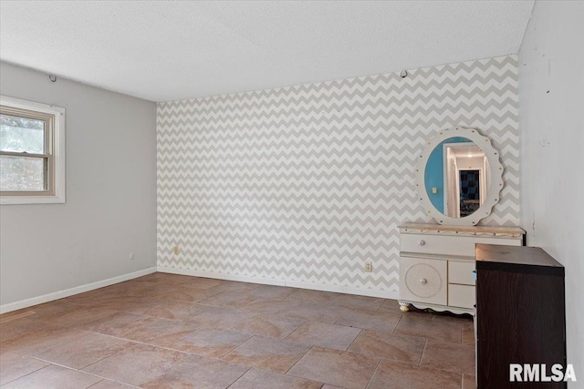 unfurnished bedroom with an accent wall, a textured ceiling, and baseboards