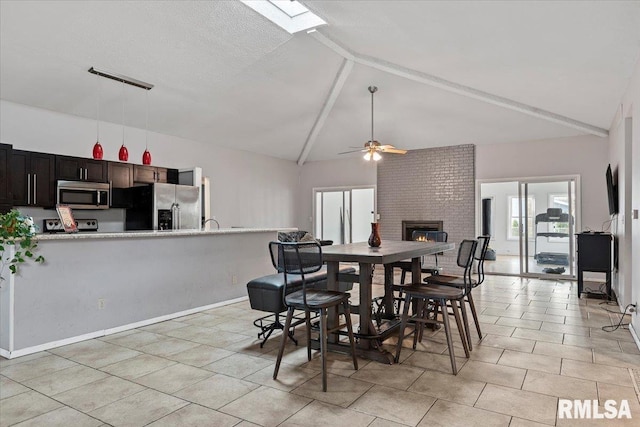 dining space with vaulted ceiling with beams, light tile patterned floors, a fireplace, and a ceiling fan