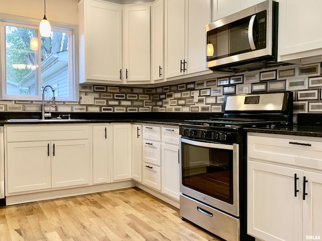 kitchen featuring stainless steel appliances, a sink, white cabinetry, light wood-style floors, and tasteful backsplash