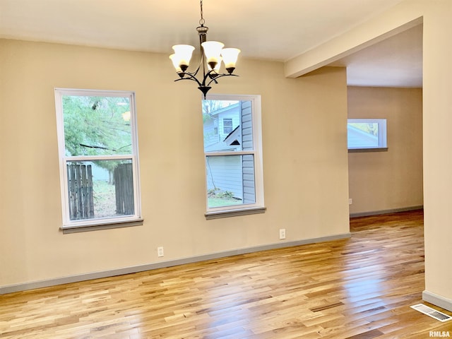 empty room featuring a notable chandelier, wood finished floors, visible vents, baseboards, and beam ceiling