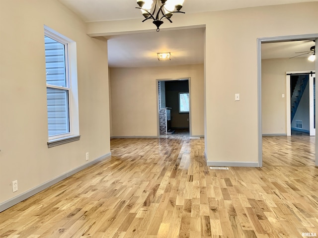 unfurnished room with light wood-type flooring, visible vents, baseboards, and ceiling fan with notable chandelier