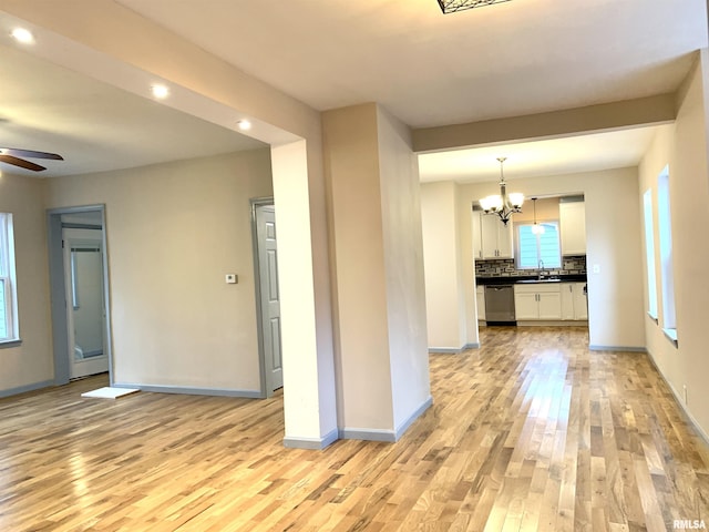 spare room featuring baseboards, light wood finished floors, and ceiling fan with notable chandelier