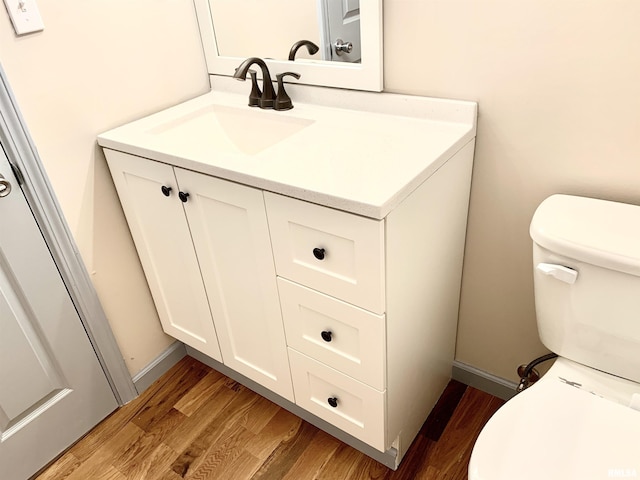 half bathroom featuring vanity, wood finished floors, toilet, and baseboards