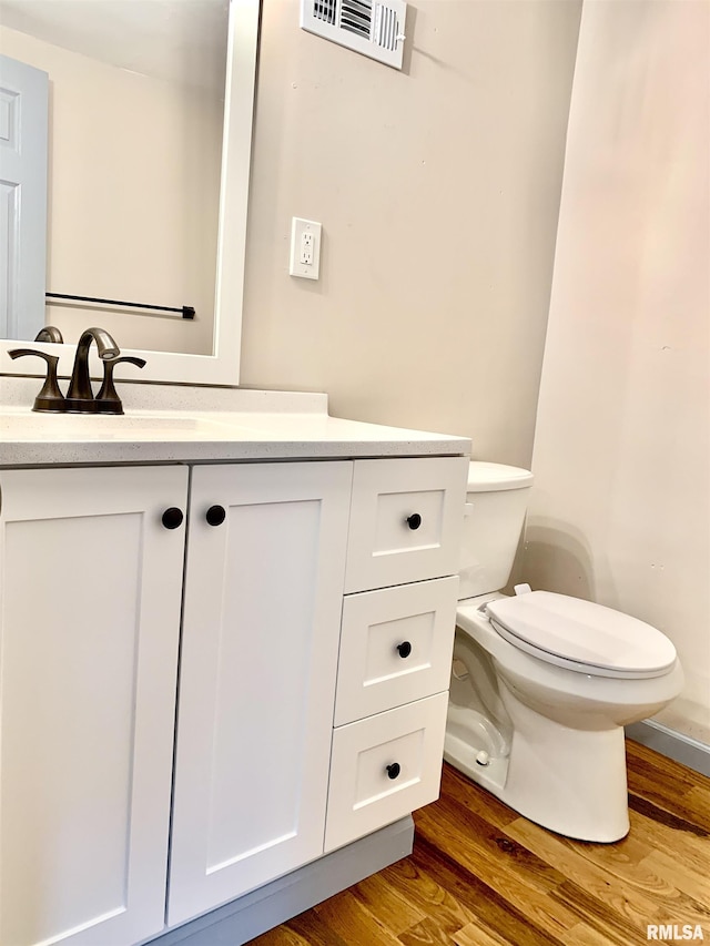 half bathroom featuring toilet, vanity, wood finished floors, and visible vents