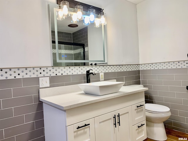 full bath featuring toilet, a stall shower, vanity, and tile walls