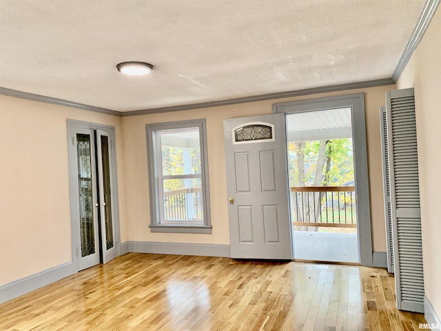 doorway to outside featuring light wood-type flooring, crown molding, a textured ceiling, and baseboards