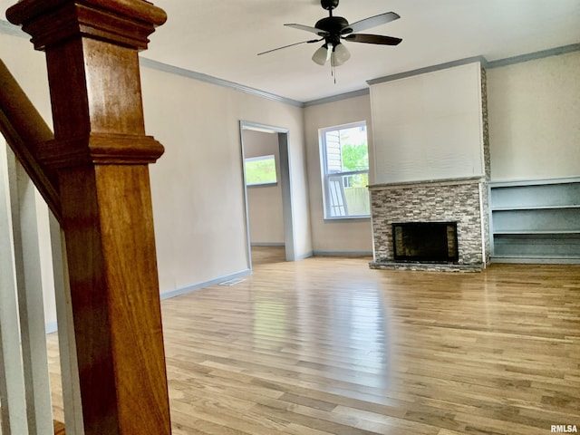 unfurnished living room with baseboards, ceiling fan, ornamental molding, a stone fireplace, and light wood-type flooring