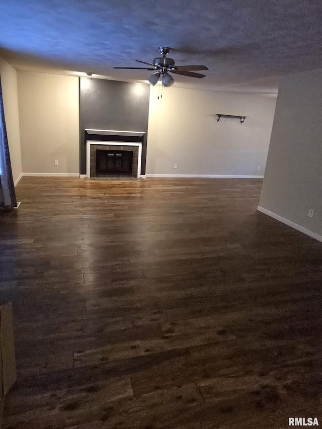 unfurnished living room featuring dark wood-style floors, ceiling fan, a tile fireplace, and baseboards