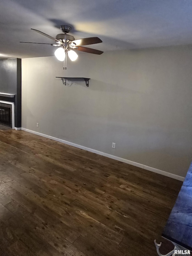 unfurnished living room featuring ceiling fan, baseboards, dark wood-style flooring, and a glass covered fireplace