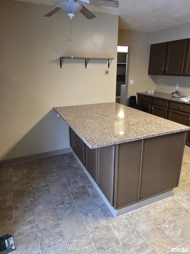 kitchen featuring ceiling fan, dark brown cabinetry, a peninsula, light stone countertops, and open shelves