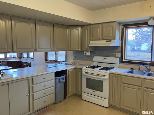 kitchen with under cabinet range hood, a sink, light countertops, decorative backsplash, and white gas range