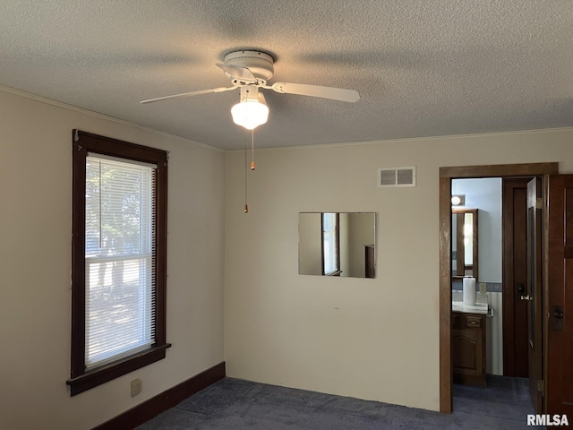 empty room featuring a textured ceiling, dark colored carpet, visible vents, and a ceiling fan