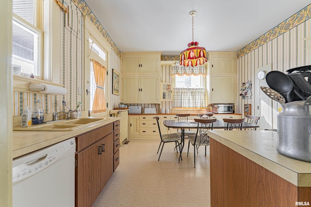 kitchen with white dishwasher, a sink, light countertops, stainless steel microwave, and wallpapered walls