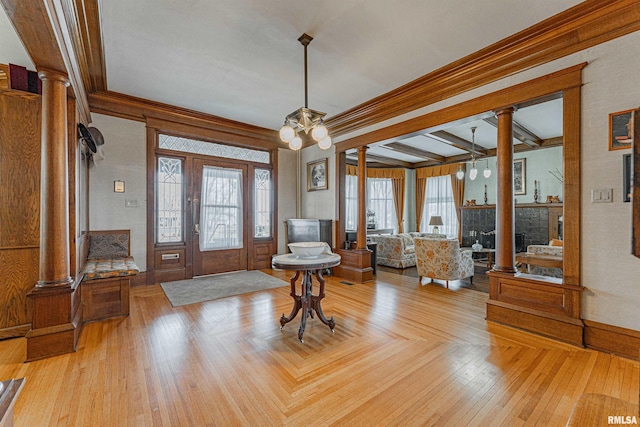 entrance foyer featuring a notable chandelier, a fireplace, parquet floors, ornate columns, and crown molding
