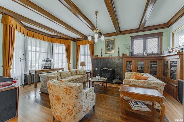 living area with a notable chandelier, a fireplace, beamed ceiling, and wood finished floors