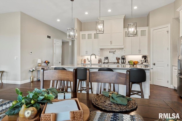 kitchen featuring a kitchen island with sink, dark wood-type flooring, white cabinetry, a kitchen breakfast bar, and decorative backsplash